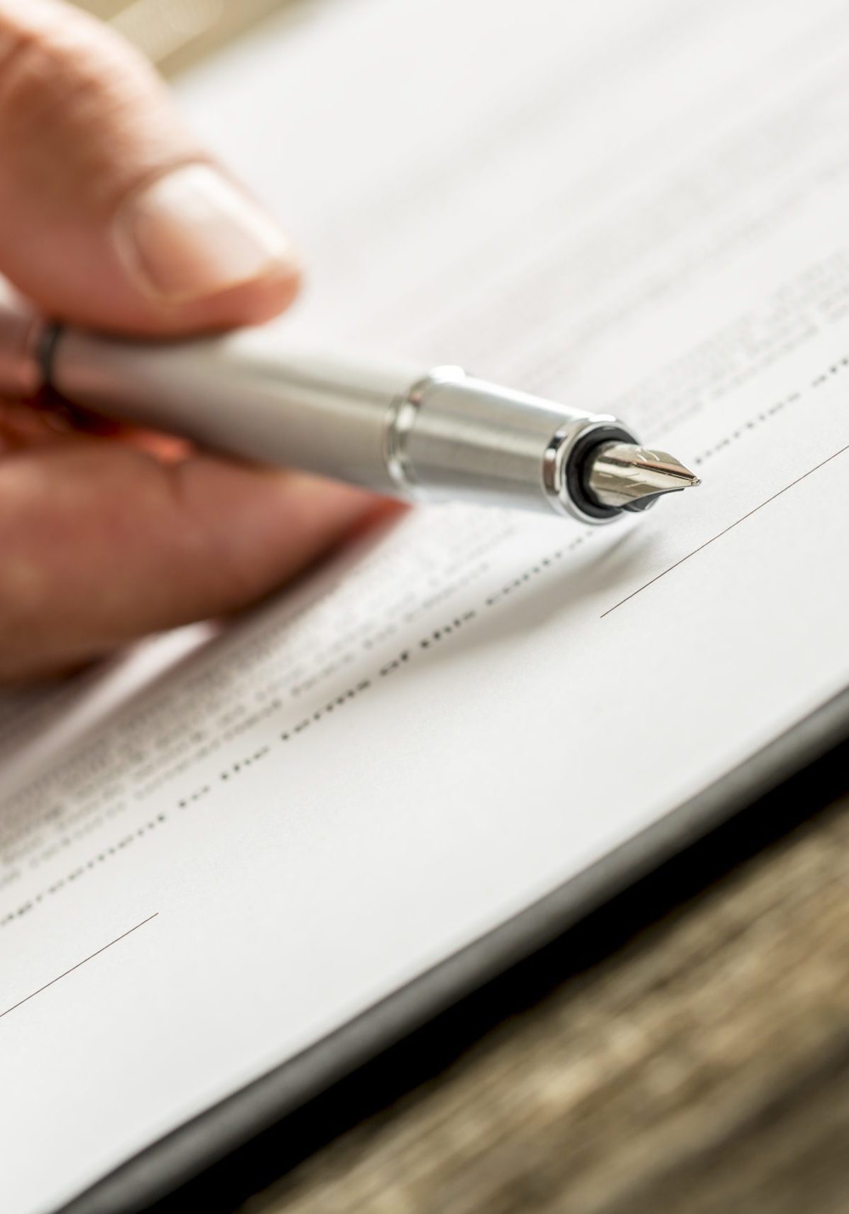 Closeup of male hand holding an ink pen pointing with its end on a line in the bottom of a contract ready for signature. Conceptual of signing contract application form or membership.